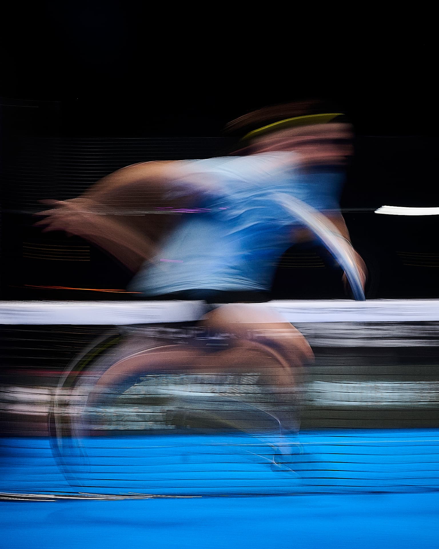 Tennis player in motion blur striking a shot on a blue court under floodlights