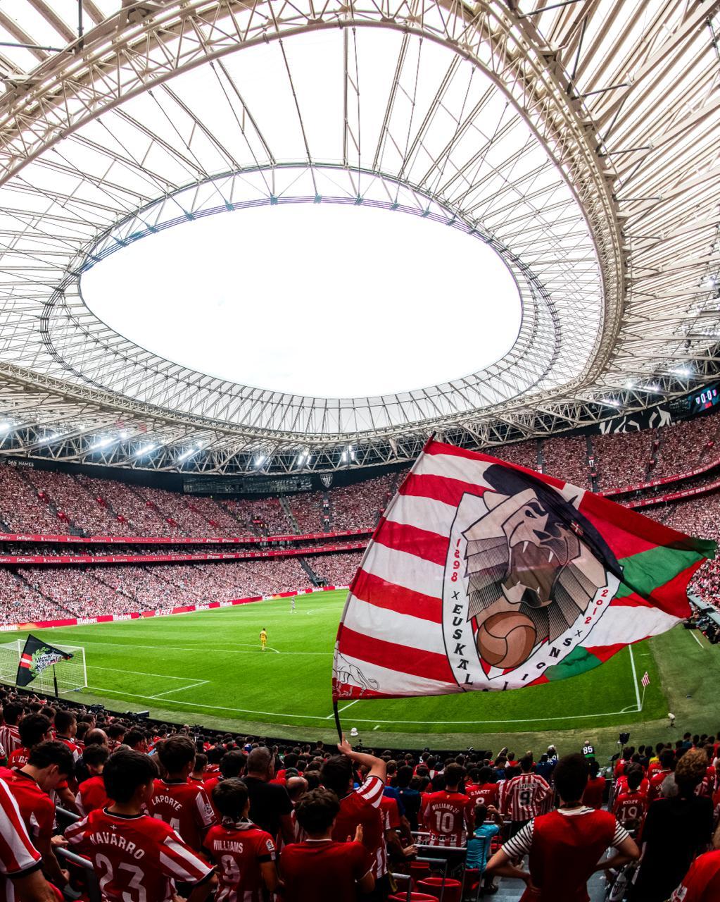 Packed stadium stand with a club flag waving over the pitch during a live match